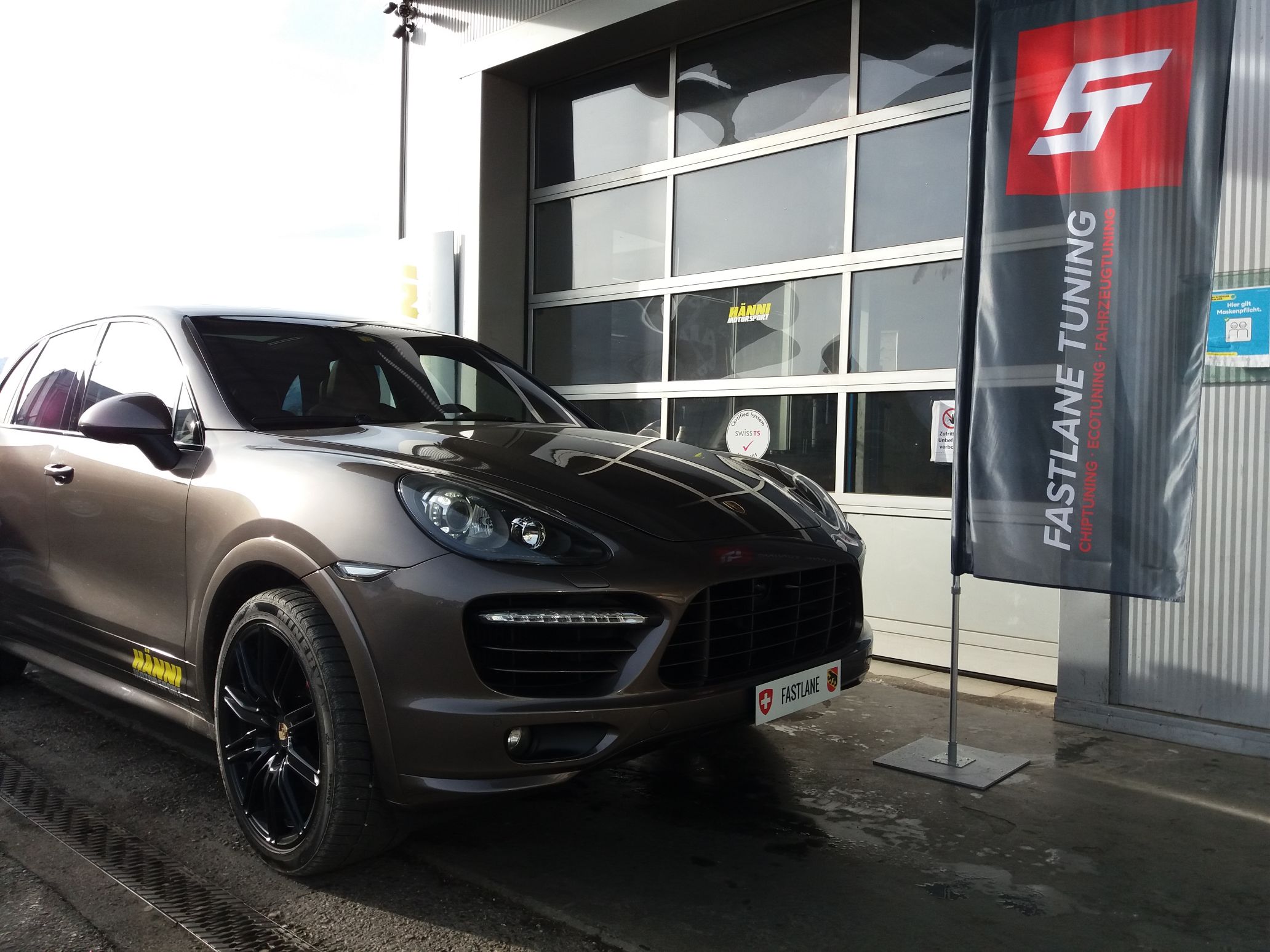 Ein brauner Porsche Cayenne Turbo S steht neben der Fastlane Tuning Schweiz Flagge.
