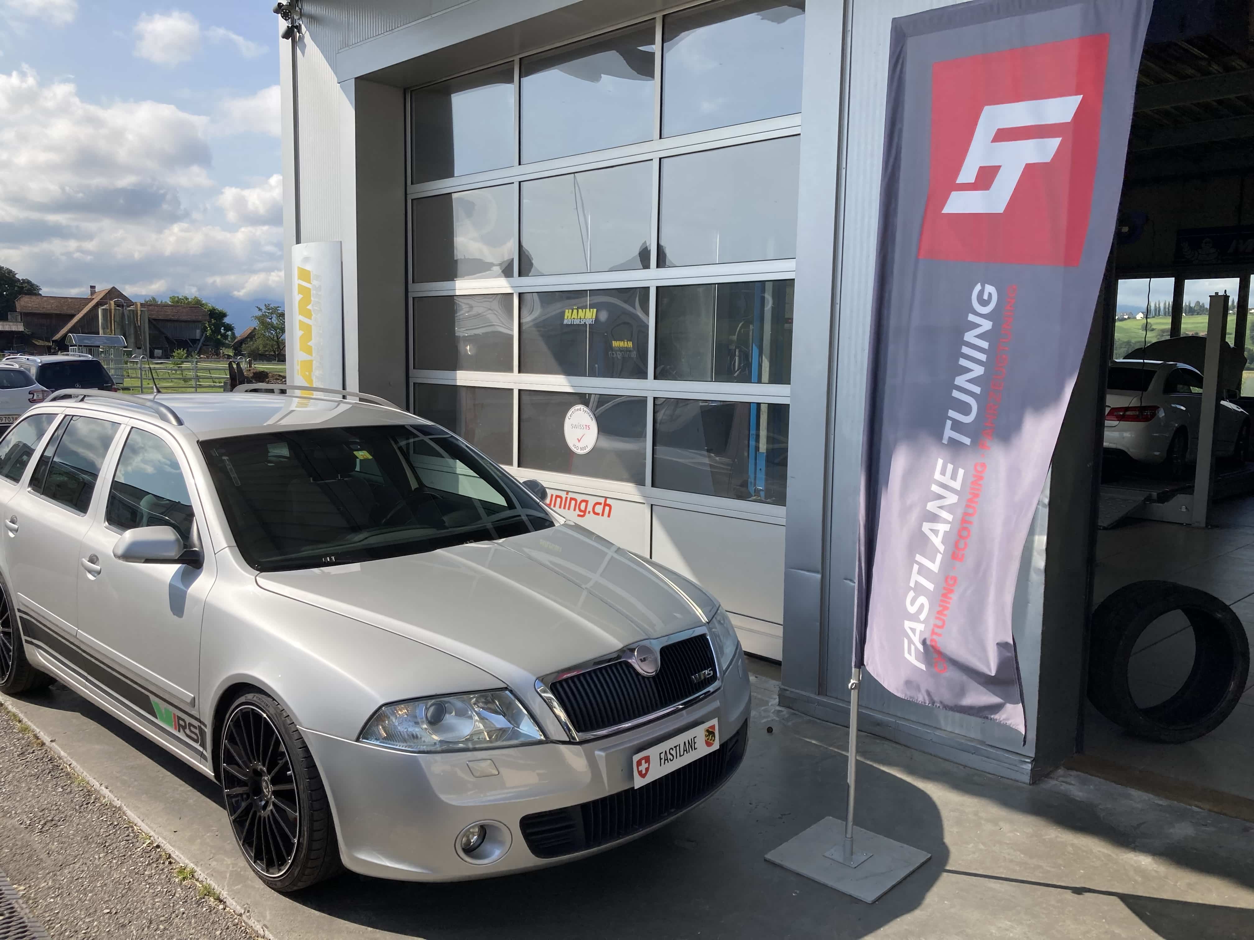 Ein silberner Skoda Octavia II RS steht vor der Garage neben der Fastlane Tuning Schweiz Flagge